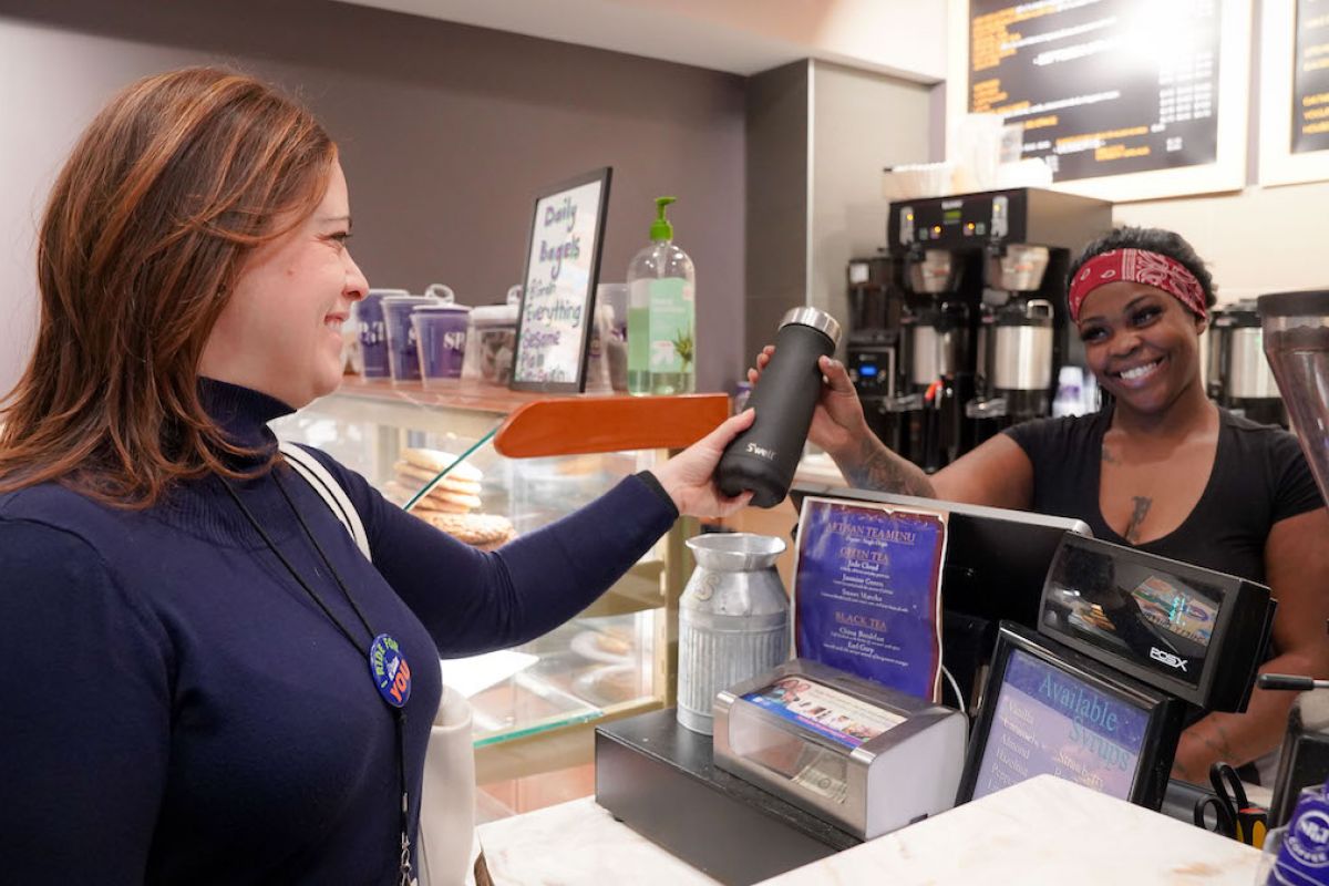 Dr. Ohm hands a stainless-steel thermos to a server at a coffee shop