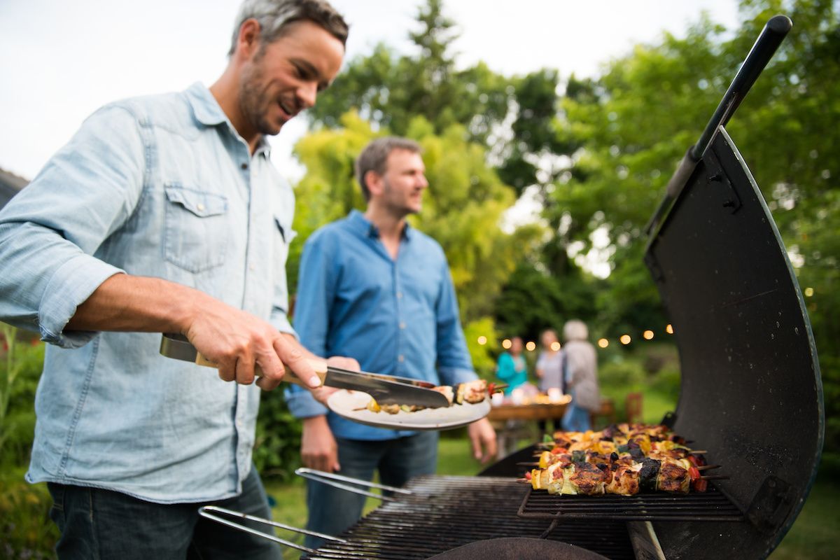 Two middle-aged men barbecuing outside