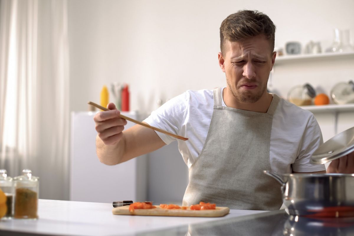 Man looks disgusted after tasting something he is cooking