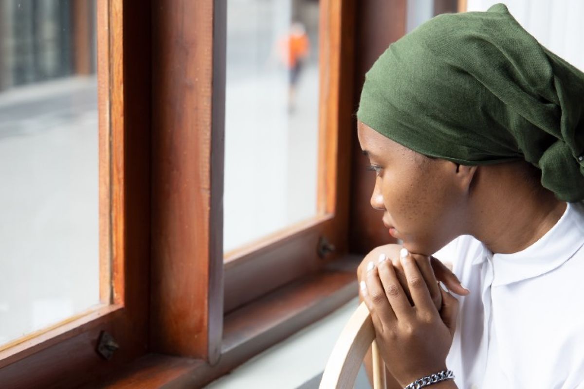 Black woman wearing a headscarf looks out the window.