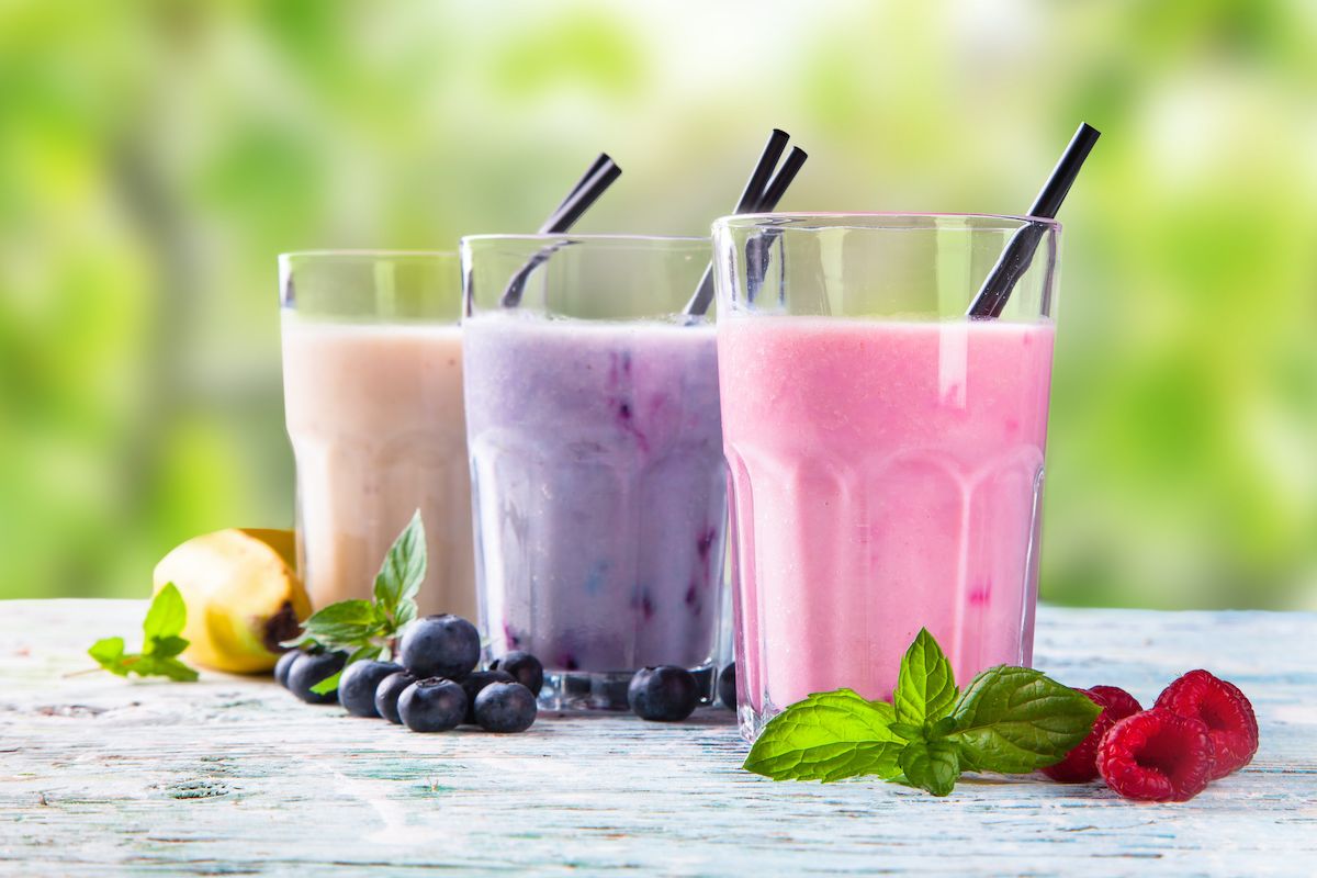 Three smoothies on a table surrounded by fruit