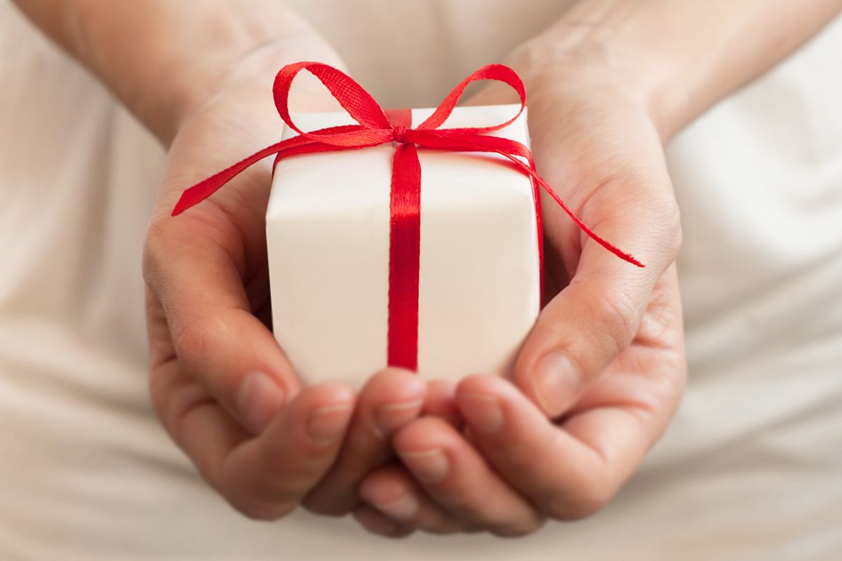 Hands holding a small present wrapped with a red bow