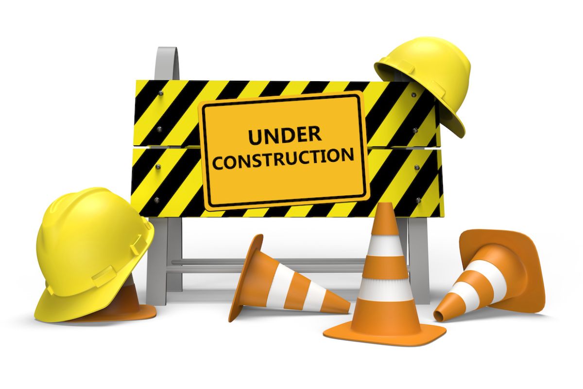 3D rendering of construction barrier with a sign that reads "under construction". Cones and construction hats are placed around the construction barrier.