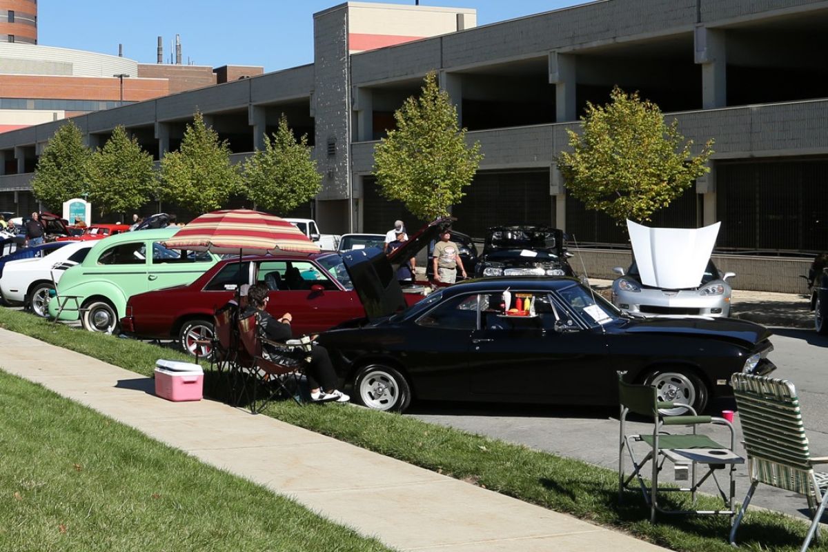 Several classic cars, many with their hoods open, are lined up in front of the main parking garage at Roswell Park Comprehensive Cancer Center. 