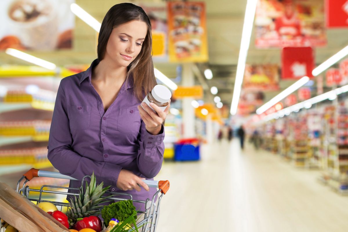 Person reading a label on a bottle while shopping in a supermarket