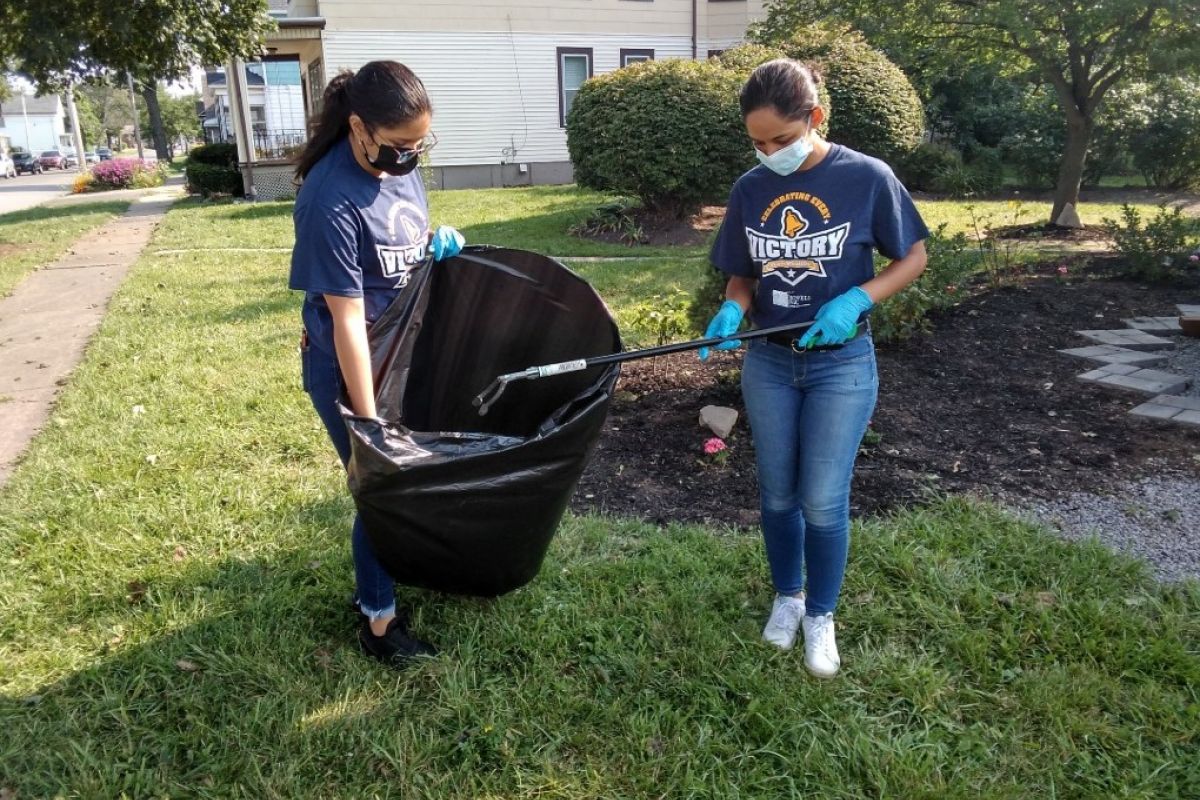 One young woman holds a large plastic garbage bag as another deposits trash while they work to clean up the Fruit Belt neighborhood. 