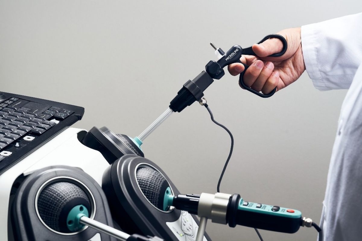 A person wearing a lab coat holds two controllers in their hands in order to conduct robot-assisted surgery