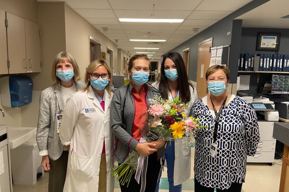 Four women wearing surgical masks stand around a woman in the center, holding flowers and being recognized as Roswell Park's Nurse of the Month for September.