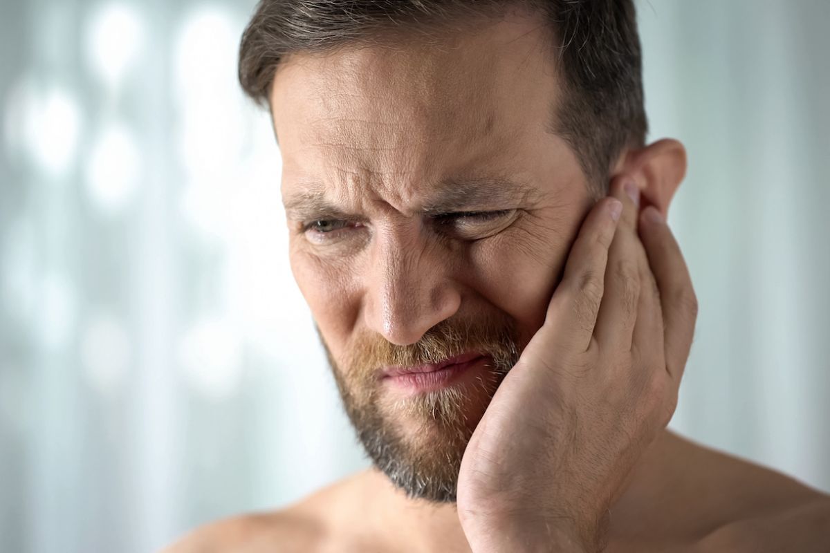 Man holds his ear and grimaces in pain - stock
