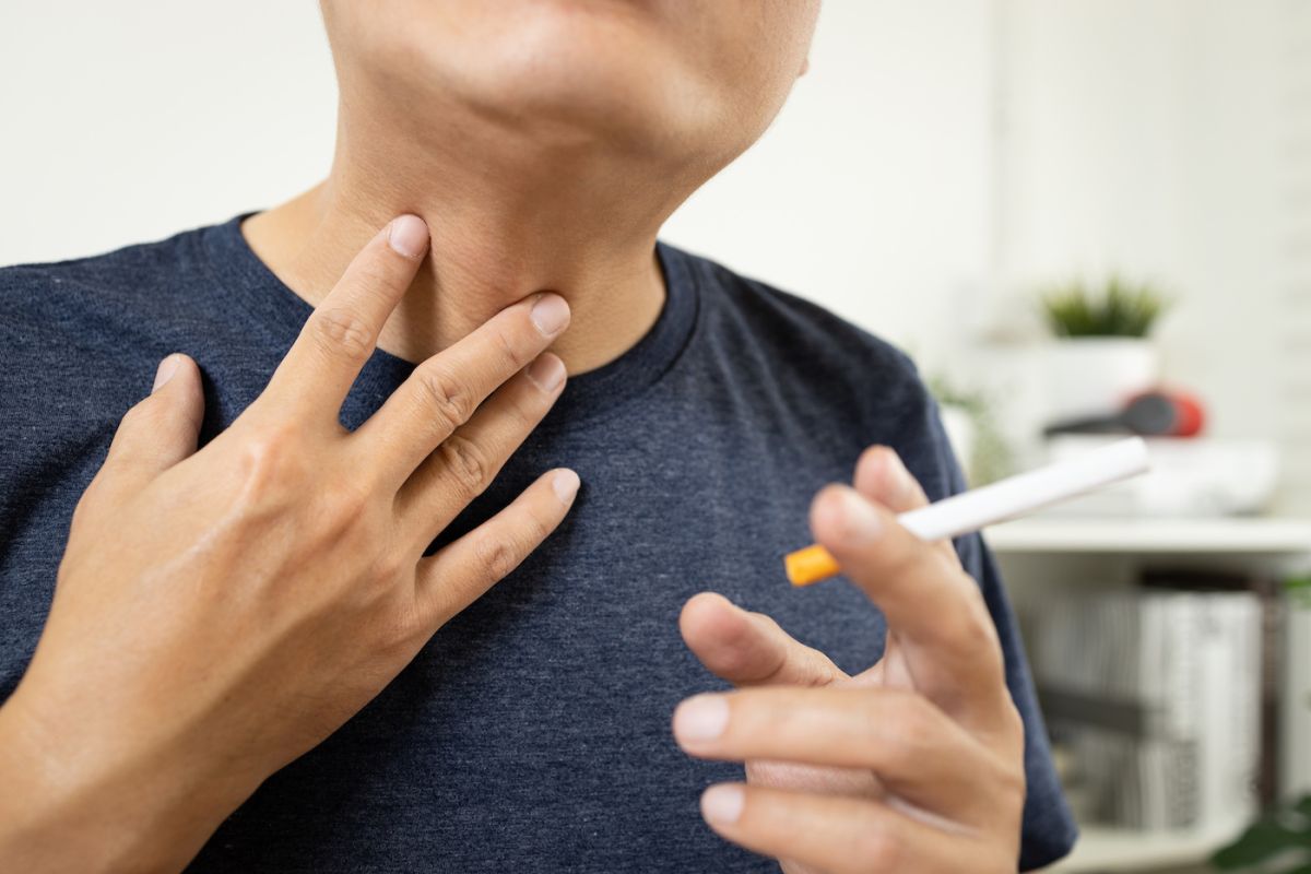 Man rubbing neck and holding cigarette 