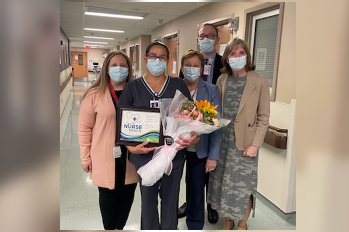 Cindy Latimore, second from left, holds a bouquet of flowers and a certificate, given to her for being named Nurse of the Month for May. She is standing in a hallway with other members of the Roswell Park staff, including President and CEO Candace S. Johnson. 