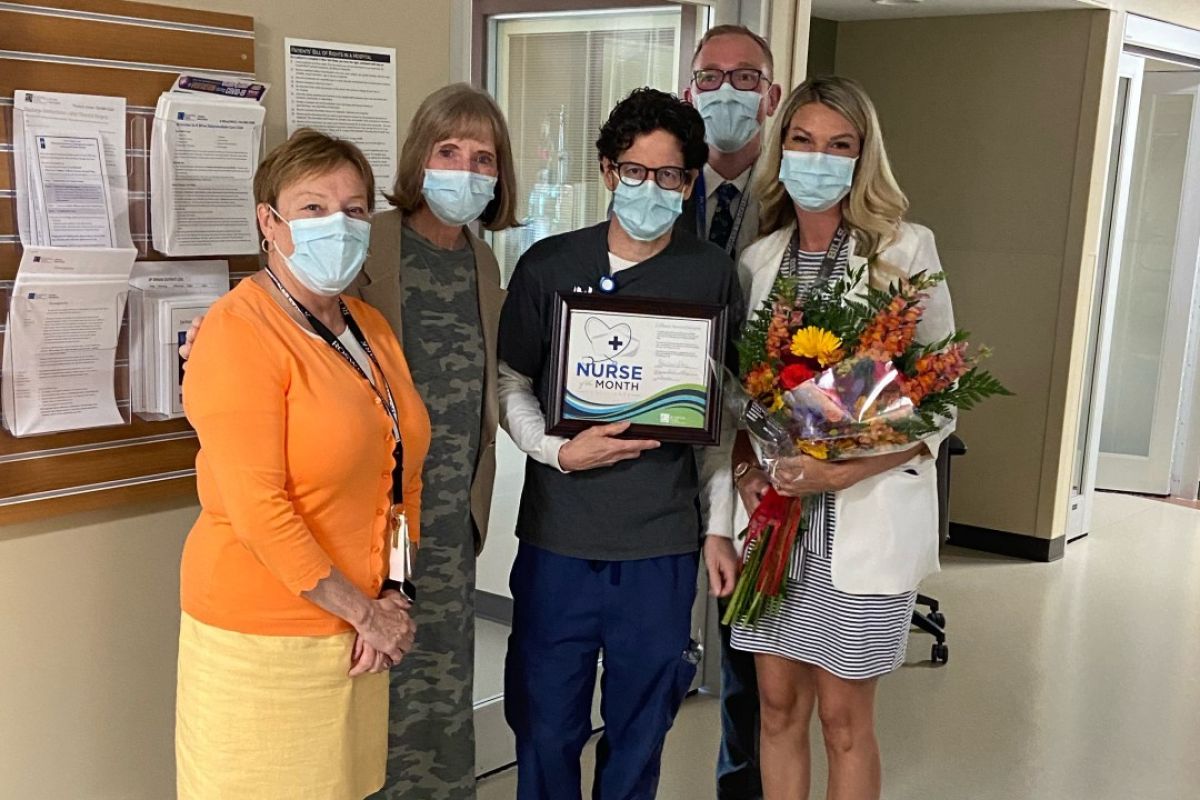 Raymond Mangione, center, holds a certificate announcing him Nurse of the Month for July. A woman to his left holds flowers. 