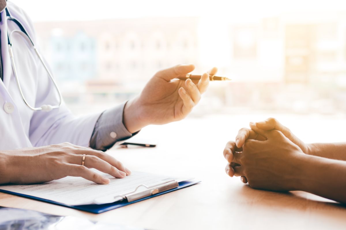 person in white coat gestures to person with clasped hands