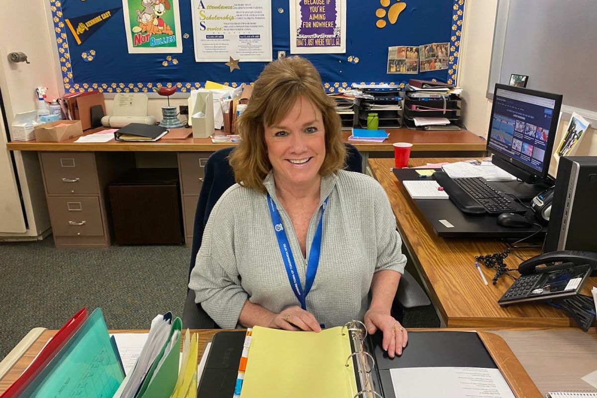 A woman sits at a desk in a school office. 