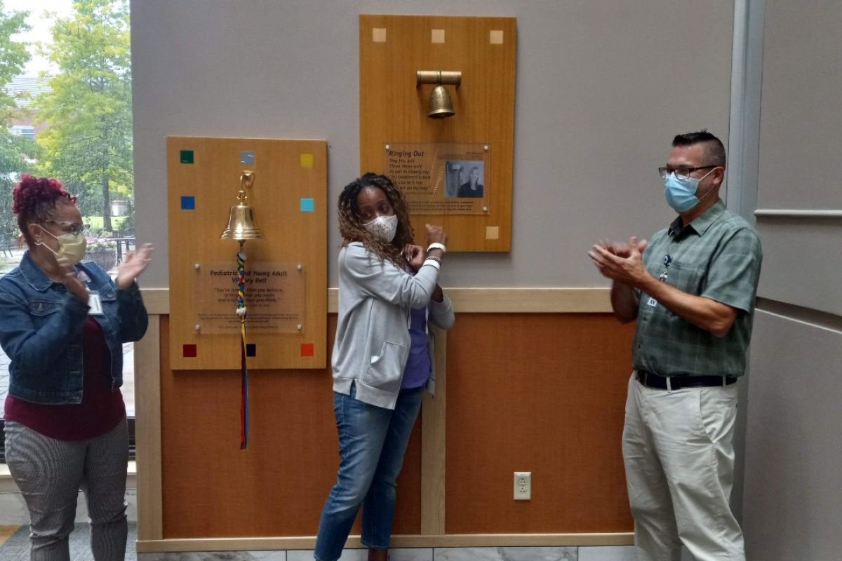 A woman in a purple hoodie rings the Victory Bell after completing a long surveillance period for cervical cancer and mesothelioma. 