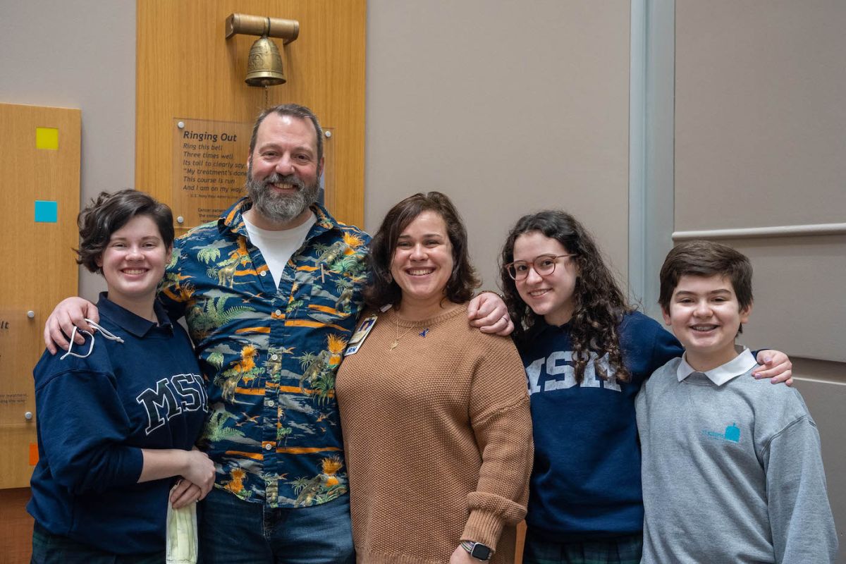 A group of five people, two adults and three children, stand before the Victory Bell.