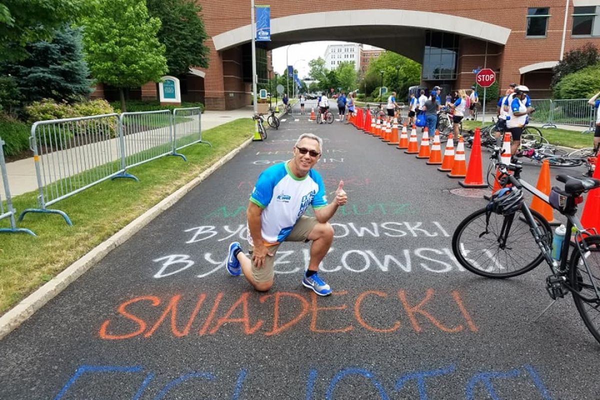 A man crouches down by his last name, written in chalk, outside Roswell Park Comprehensive Cancer Center, during the week leading up to the Ride for Roswell. 