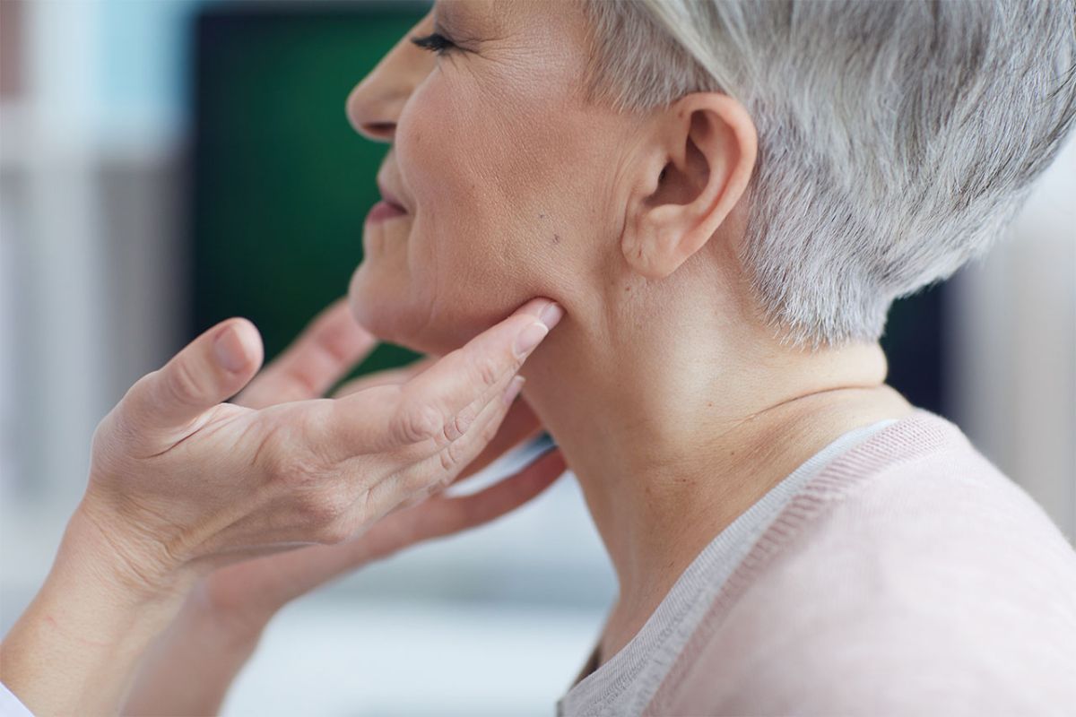 older female patient with short hair, chin slightly raised so physician can examine her throat