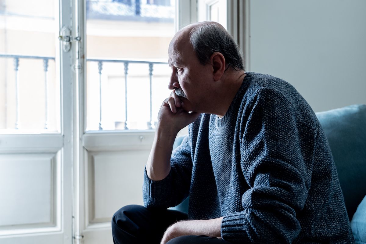 Older man looks solemnly out of a window