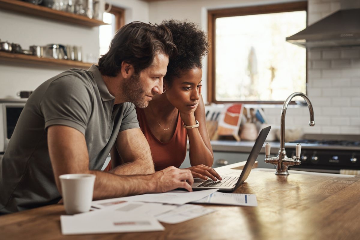 Young couple looking at a laptop in their kitchen going over finances