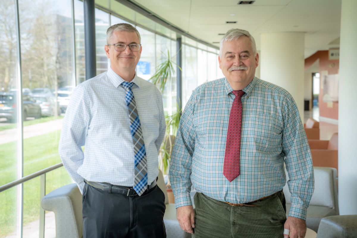 Two men in ties stand smiling in a sunlit lobby