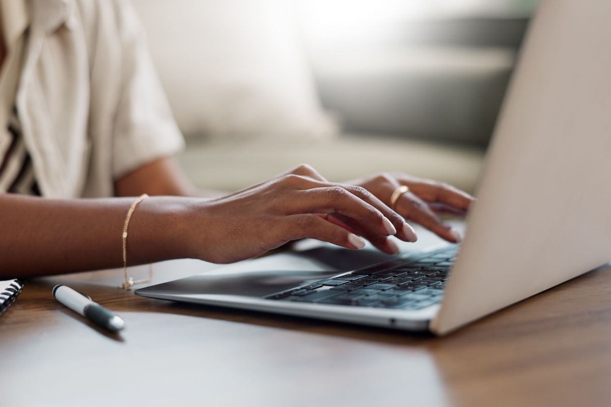 Close up of a person's hands typing onto a computer while sitting at a desk.