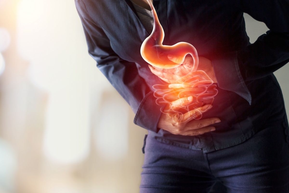 Person holding their stomach in pain with a drawing of the digestive system