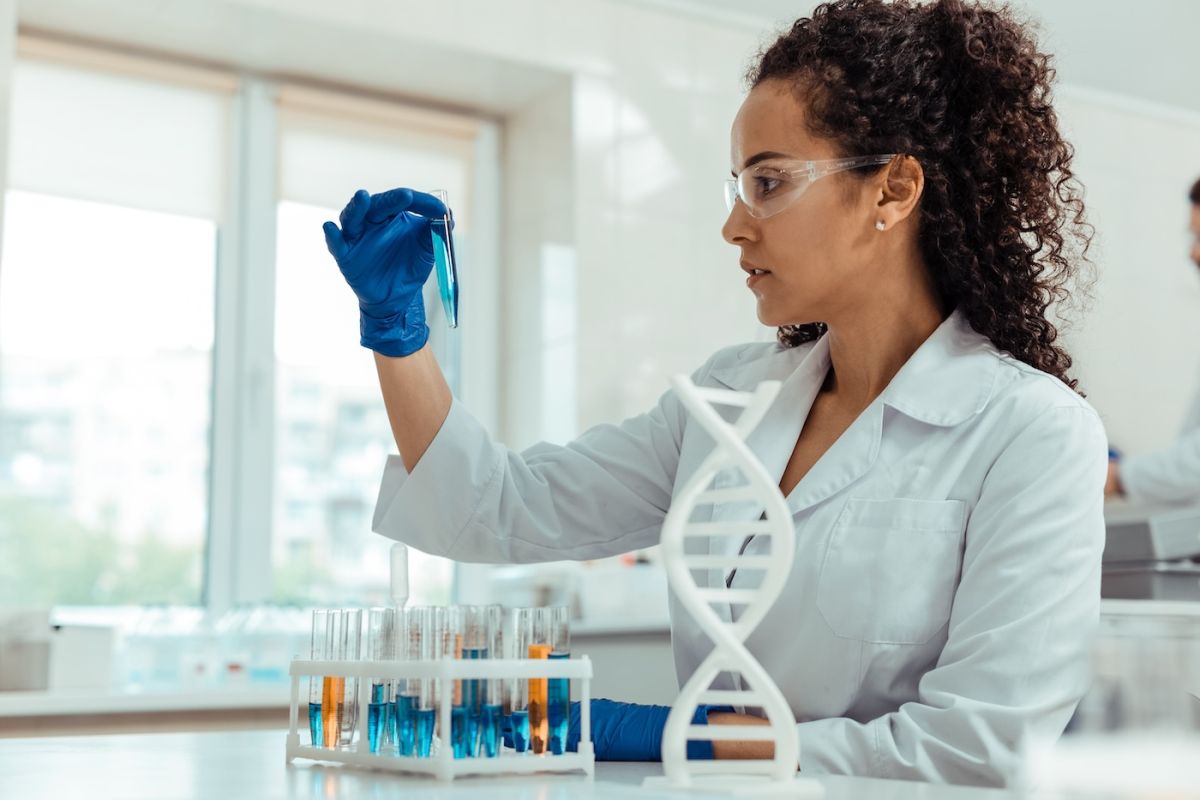 Scientist in a lab holding a beaker of liquid with a DNA strand next to her 