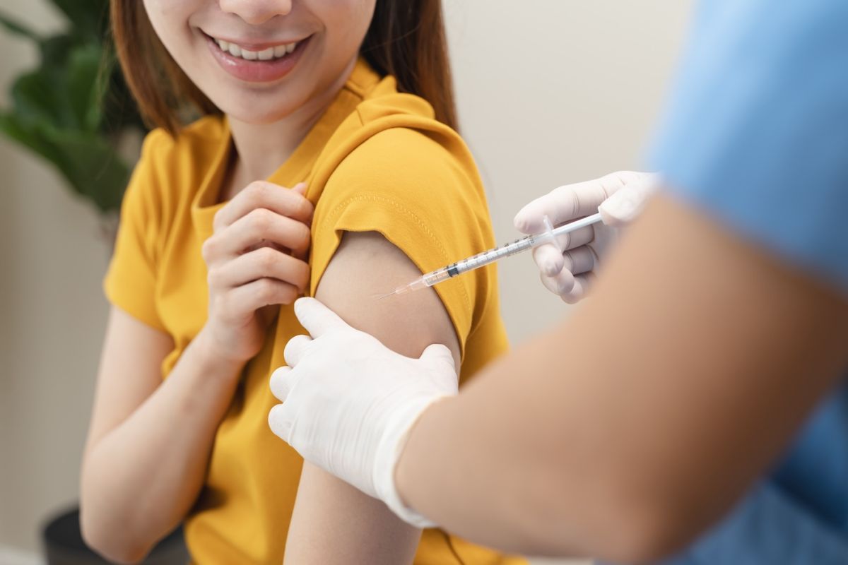 A younger girl in a yellow shirt receives a vaccine