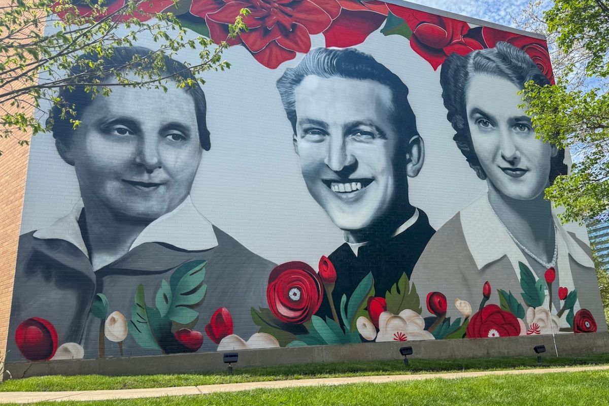 An outdor mural shows three faces in black and white framed in red and green flowers