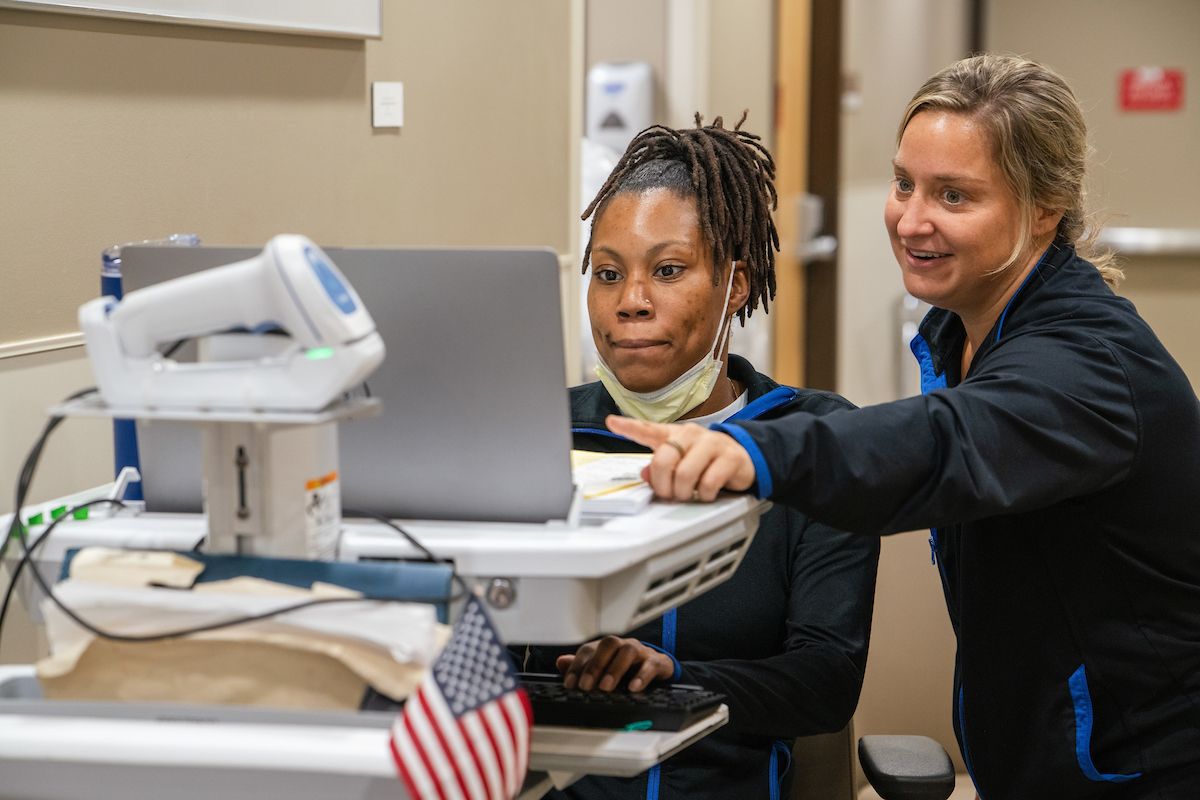 Two nurses look at patient info on a computer screen