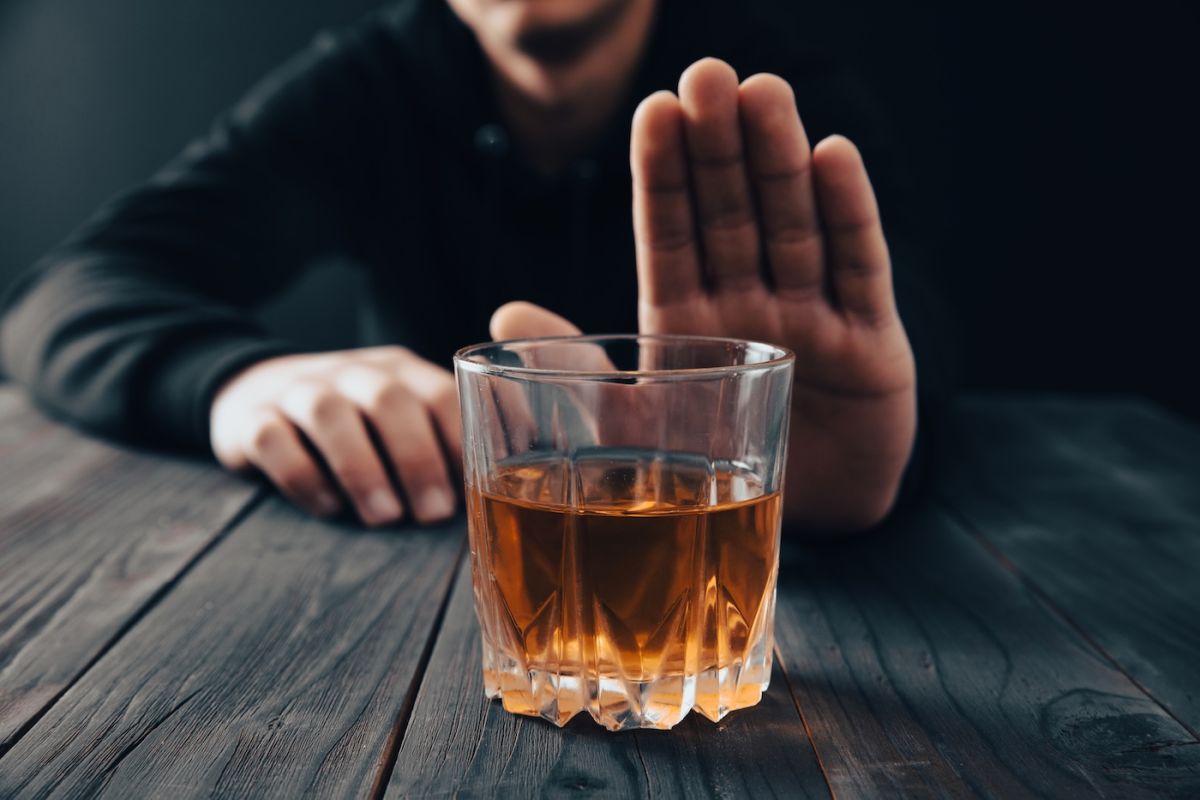 Man puts his hand up and refuses a glass of alcohol 
