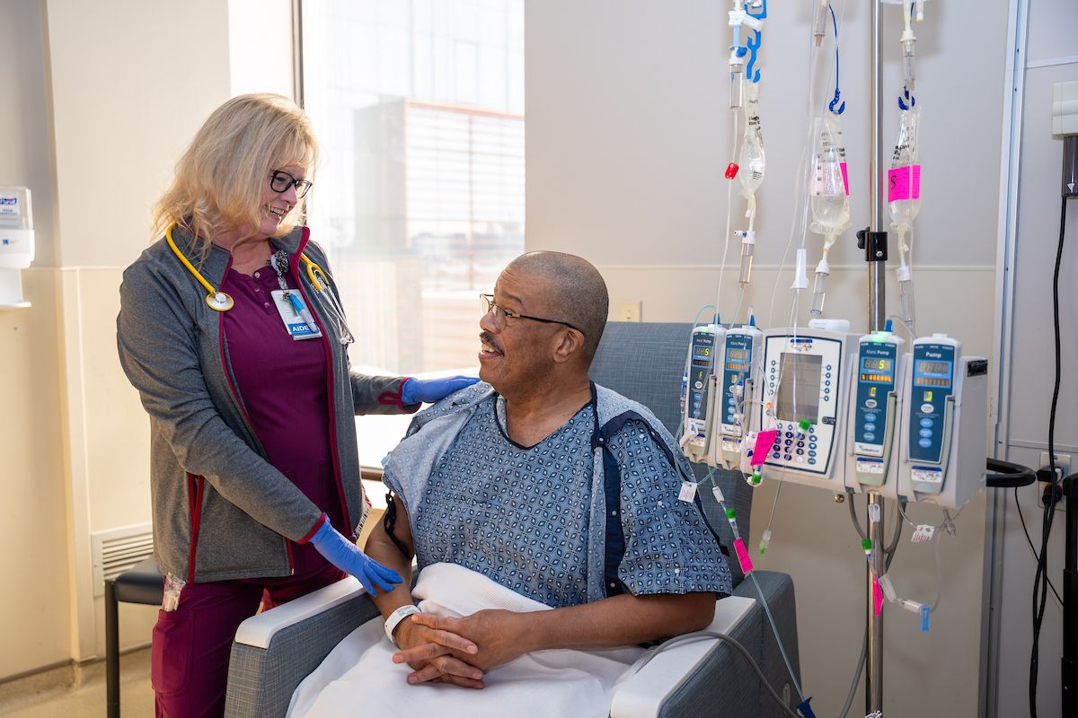 A nurse smiles at her patient in a clinic room while he receives treatment