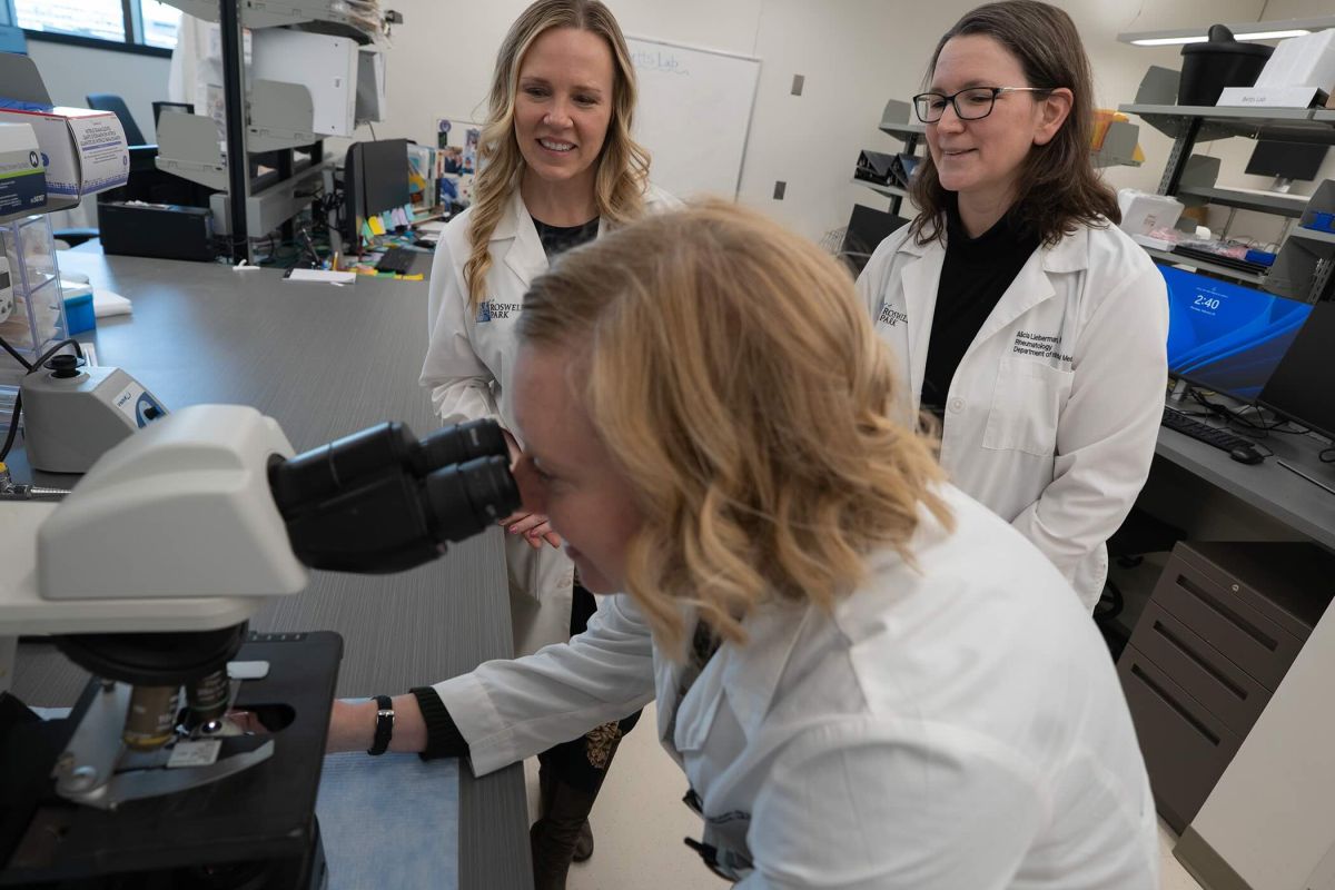 Two doctors look on as another doctor uses a microscope