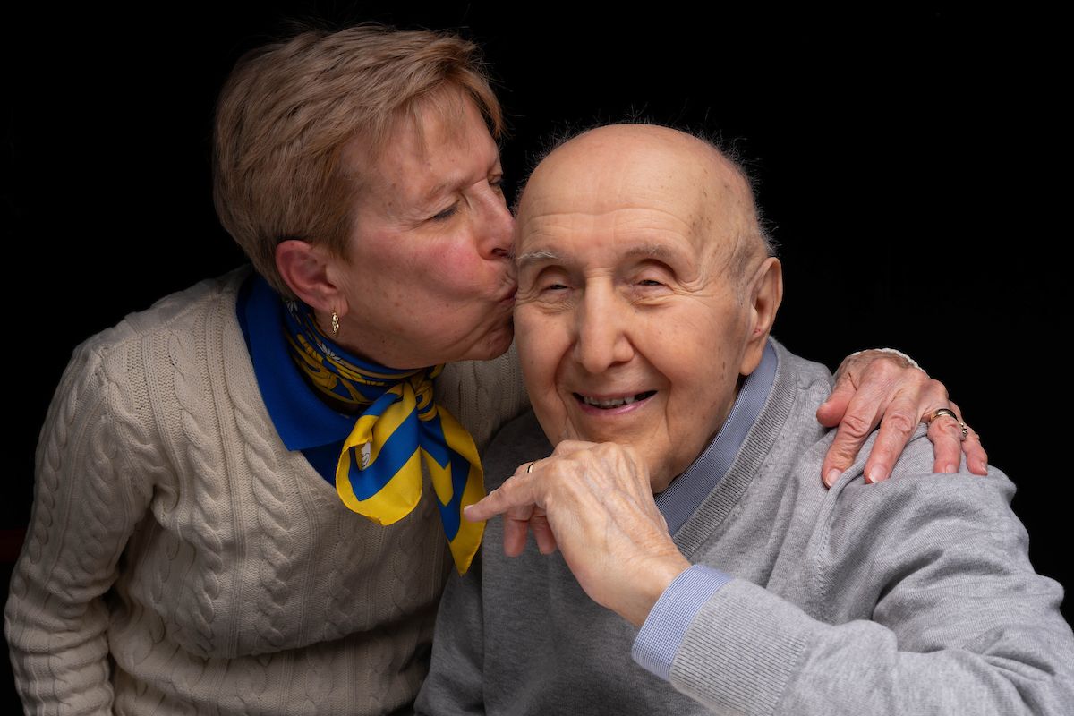 A woman leans in to place a kiss on the forehead of her husband. 
