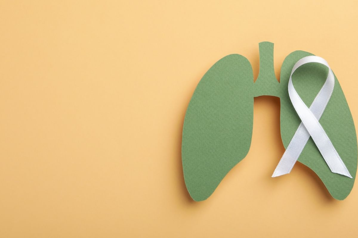 A cut out of a drawing of lungs sits on an orange background with a cancer ribbon laid overtop 