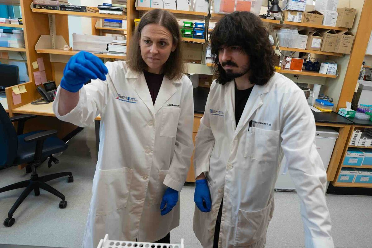A man and woman in lab coats look at a vial