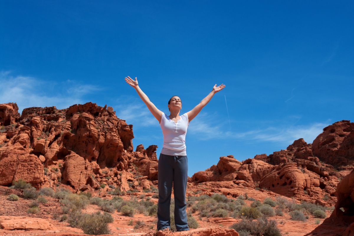 Woman standing in the desert raising her hands up into the air