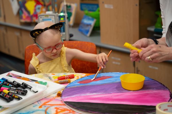 Roswell Park pediatric patient Everly focuses on her painting in the pediatric clinic, guided by the pediatric Resident Artist.