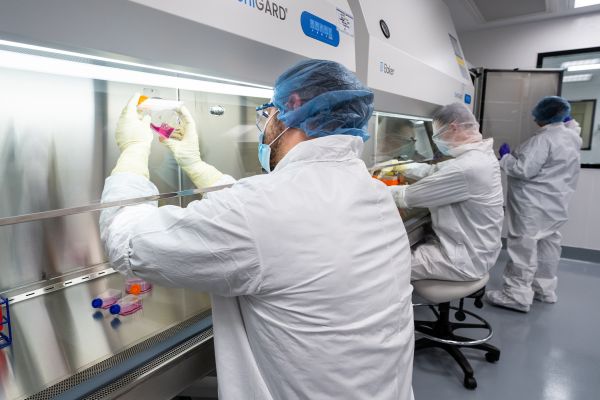 Scientists in white coats and protective gear work in lab