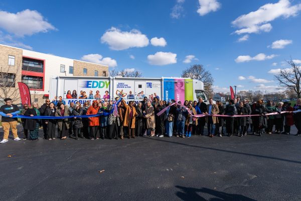 About 24 people stand in a row holding ribbon in front of a colorful truck