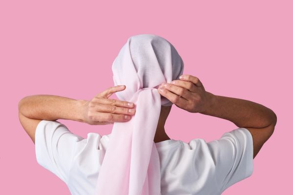 A woman ties a pink head scarf behind her head 