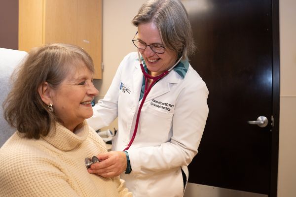 Dr. Karen McLean listens to a female patient's heart with a stethoscope in clinic