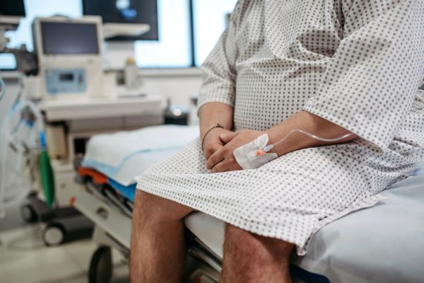 Torso of a man in a hospital gown sitting on a medical bed