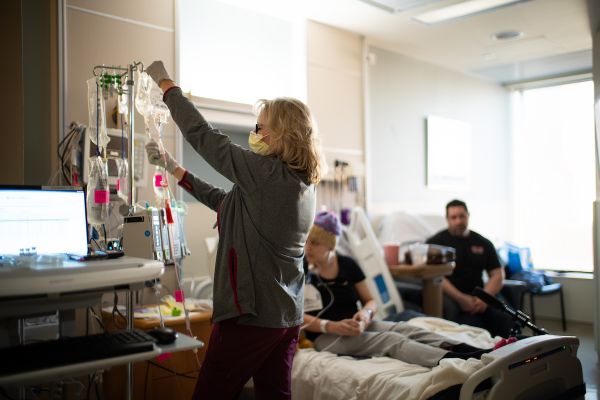 A nurse hangs infusion bags in a patient's hospital room while family member looks on