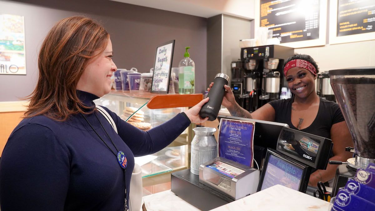 Dr. Ohm hands a stainless-steel thermos to a server at a coffee shop