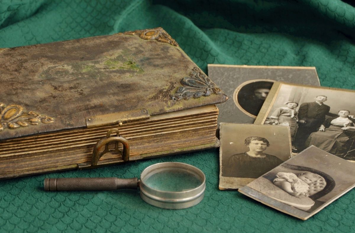 Antique photo album on a  green tablecloth with photos and a small magnifying glass next to it
