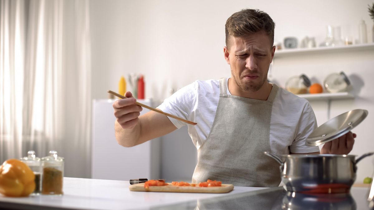 Man looks disgusted after tasting something he is cooking