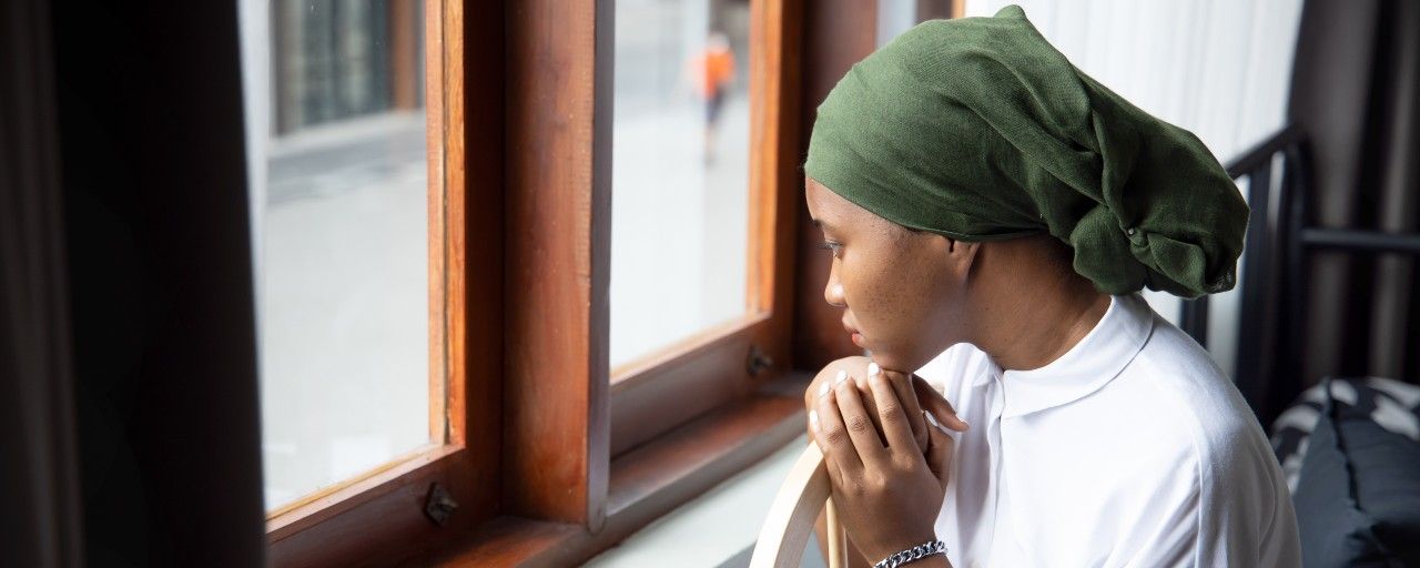 Black woman wearing a headscarf looks out the window.