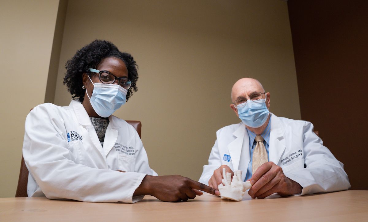 Two physicians point to a model showing the inside of a woman's neck